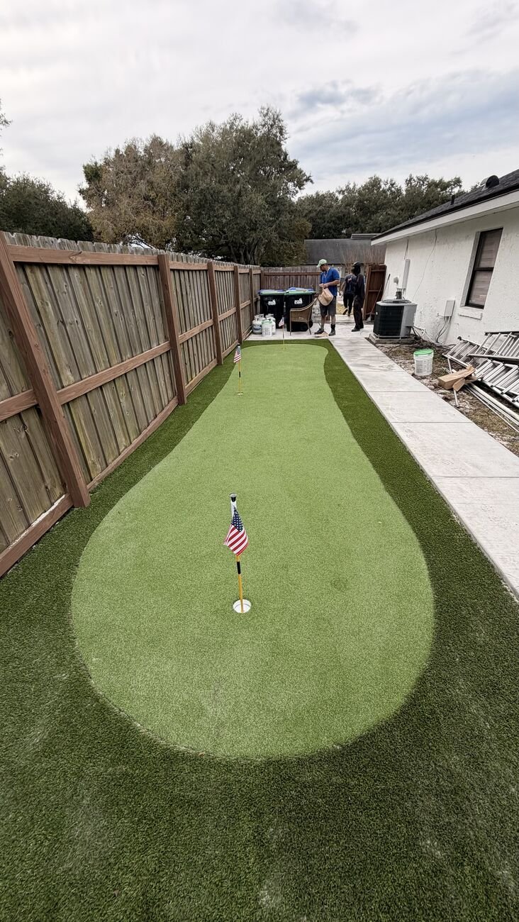 Putting green estreito na lateral da casa, ao lado da cerca de madeira