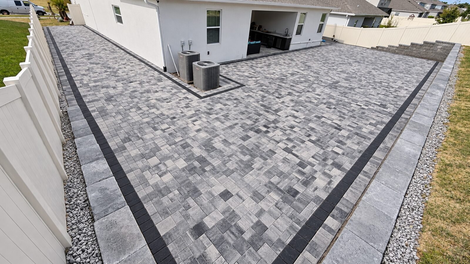 Gran patio de adoquines con muro de contención en el patio trasero, instalado por Cavisa Solutions