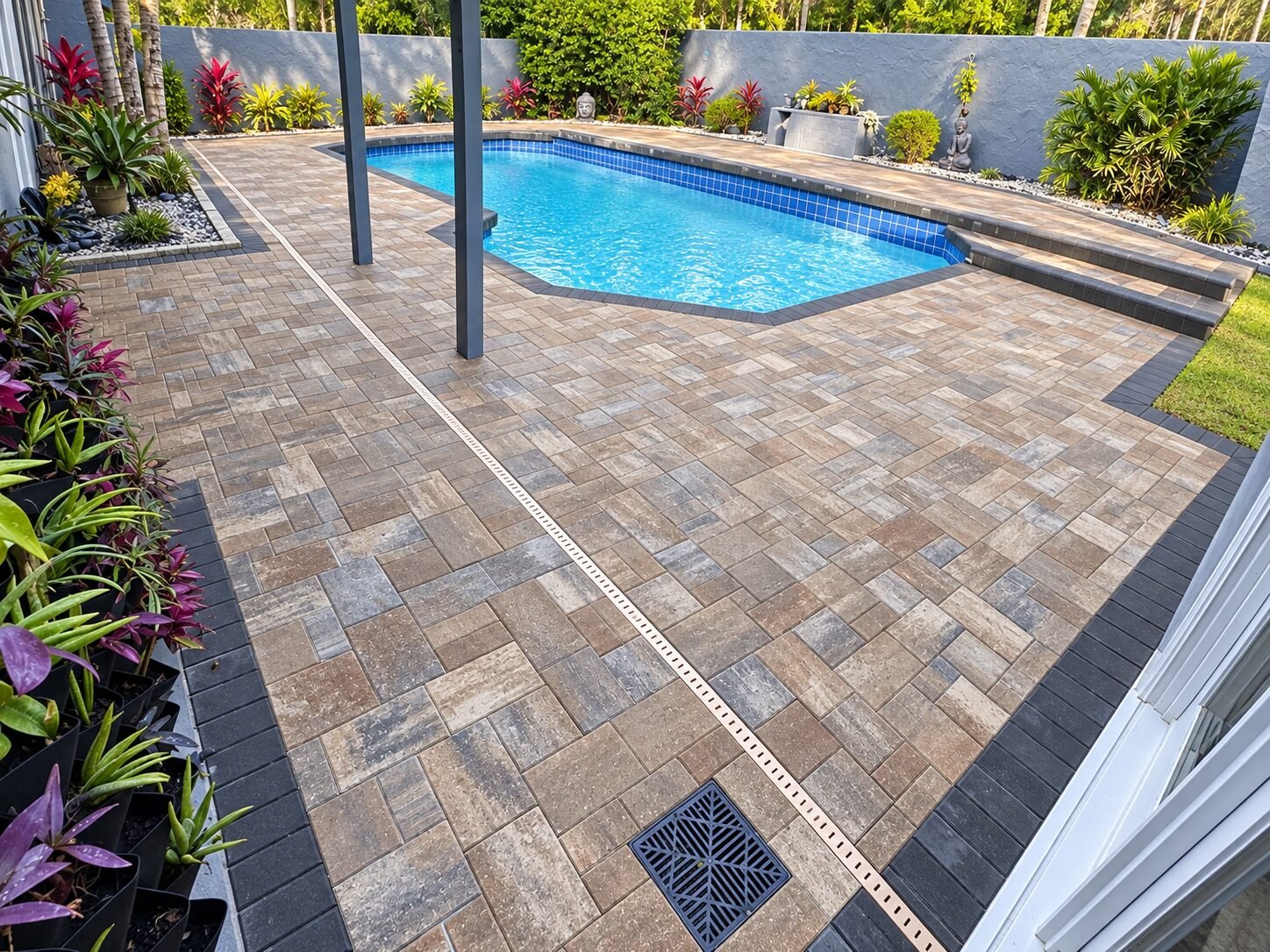 Borde de piscina de adoquines beige en un patio trasero tropical, instalado por Cavisa Solutions